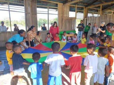 A group of teachers and children play with a play parachute