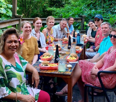 Group of people seated around an outdoor table having lunch and smiling at the camera