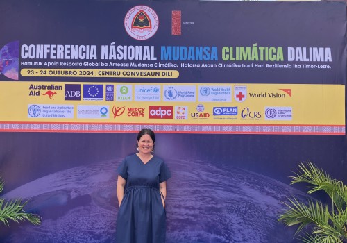 Woman smiling and standing in front of the billlboard of the National Climate Change Conference in Timor-Leste