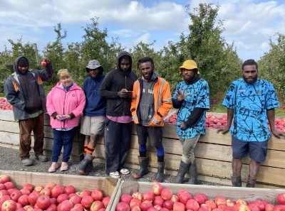 A group of people stand behind punnets of apples while smiling for the camera